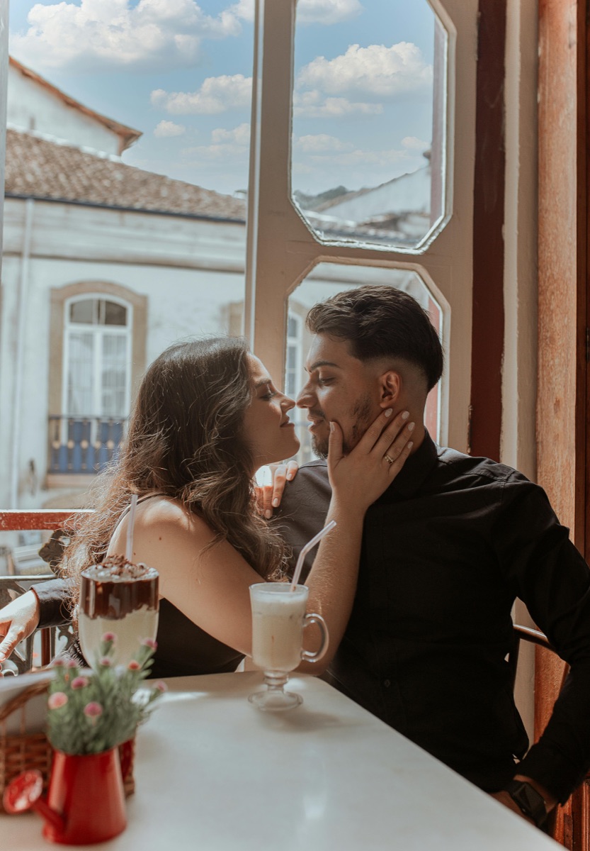 Mara and Jules leaning in close over coffee at a sunlit café window.