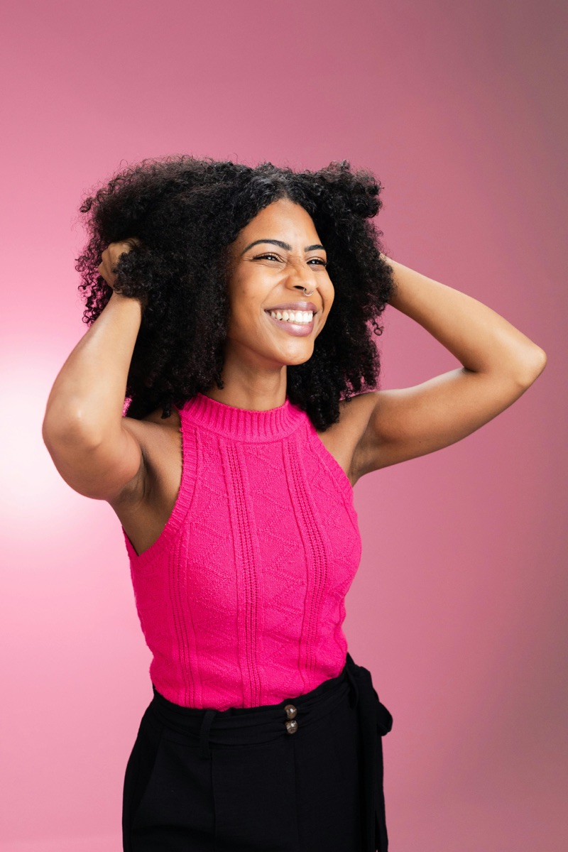 Samira laughing with her hands in her hair against a pink backdrop.
